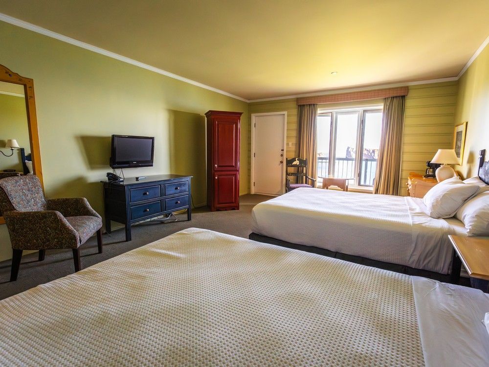 Hotelkamer van Hotel Le Mirage met twee bedden, een blauwe commode, een tv en openslaande deuren naar het balkon in een geelgroene kamer.