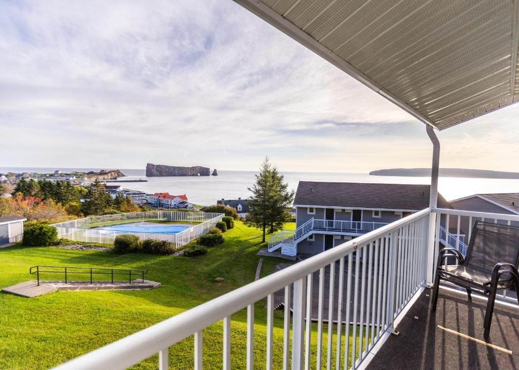 Overdekt balkon met uitzicht van Hotel Le Mirage op een park aan het meer, een eiland in de verte en het kalme water bij zonsondergang.