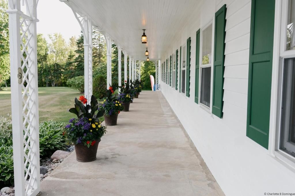 Lange witte veranda met groene luiken en potplanten langs het pad bij Hotel Tadoussac.