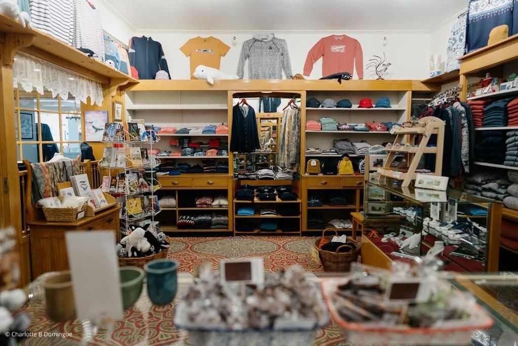 Interieur van een kleding- en cadeauwinkel met schappen vol kleding, accessoires en diverse andere artikelen.