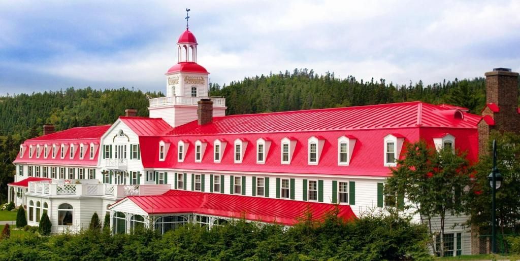 Hotel Tadoussac met een felrood dak en koepel, gelegen tegen de achtergrond van altijdgroene bomen en bergen.