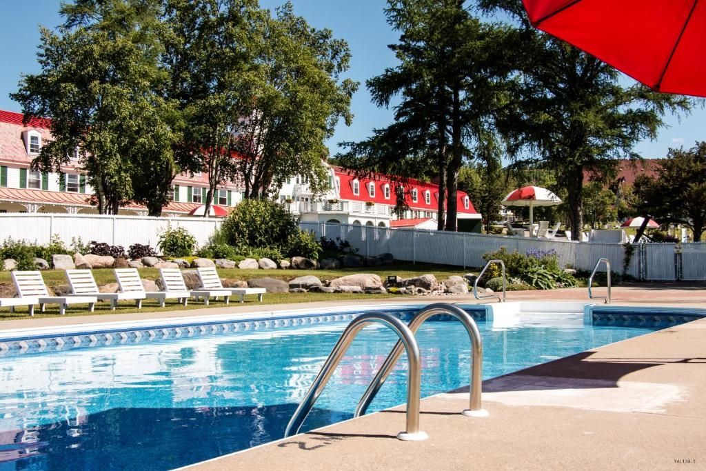 Buitenzwembad met ligstoelen, bomen en gebouwen van Hotel Tadoussac met rode daken op de achtergrond.