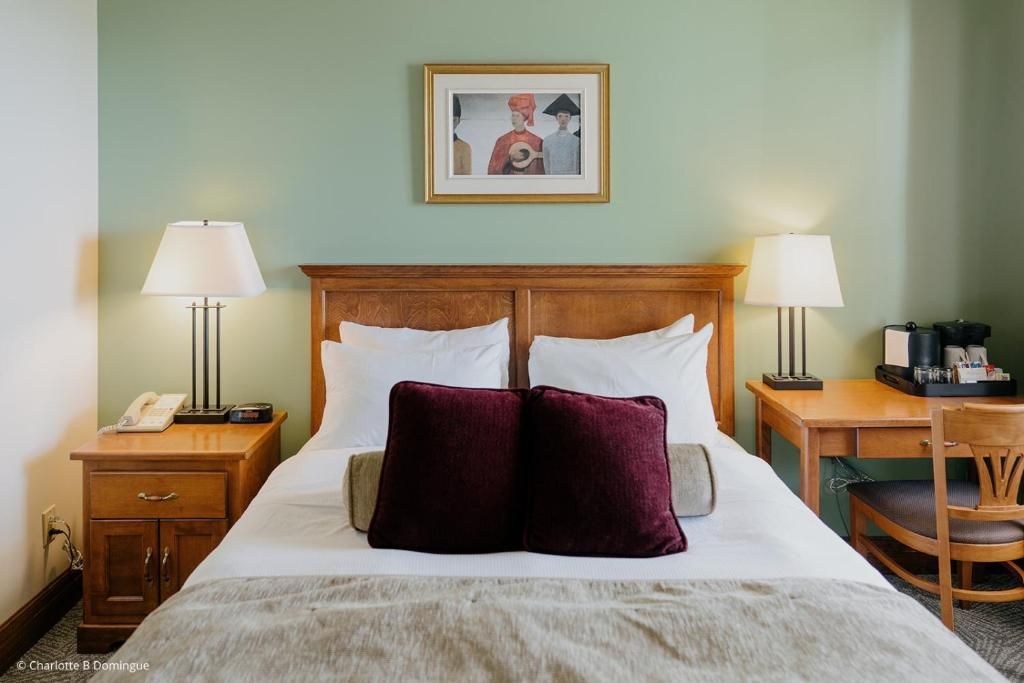 Gezellige hotelkamer van Hotel Tadoussac met een houten bed, wit beddengoed, bordeauxrode kussens en bijpassende nachtlampjes.