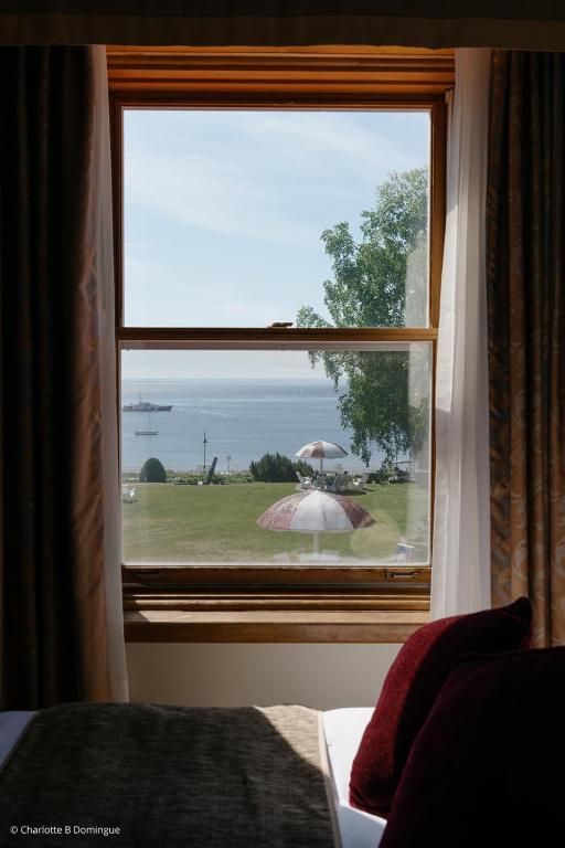 Uitzicht vanuit een slaapkamerraam van Hotel Tadoussac op een gazon aan het meer met bomen en een kleine steiger onder een heldere hemel.