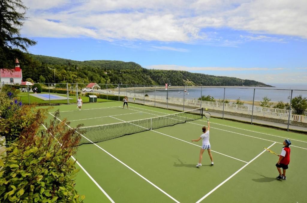 Twee mensen spelen tennis op een groene baan aan het water onder een stralende zon.