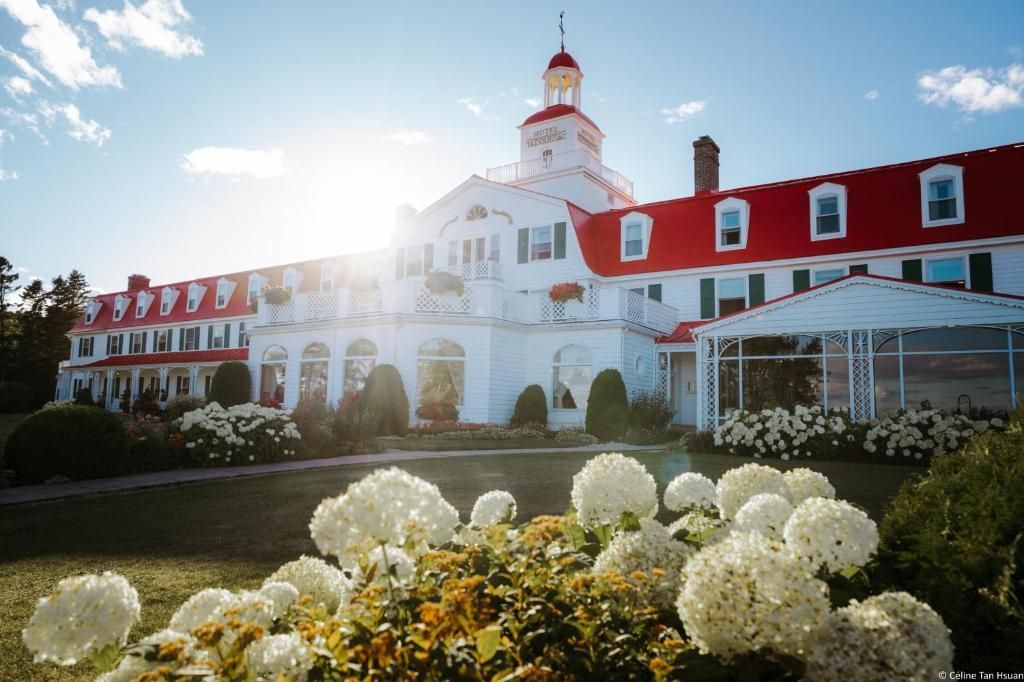 Zonovergoten Hotel Tadoussac met rood dak en bloeiende witte bloemen op de voorgrond