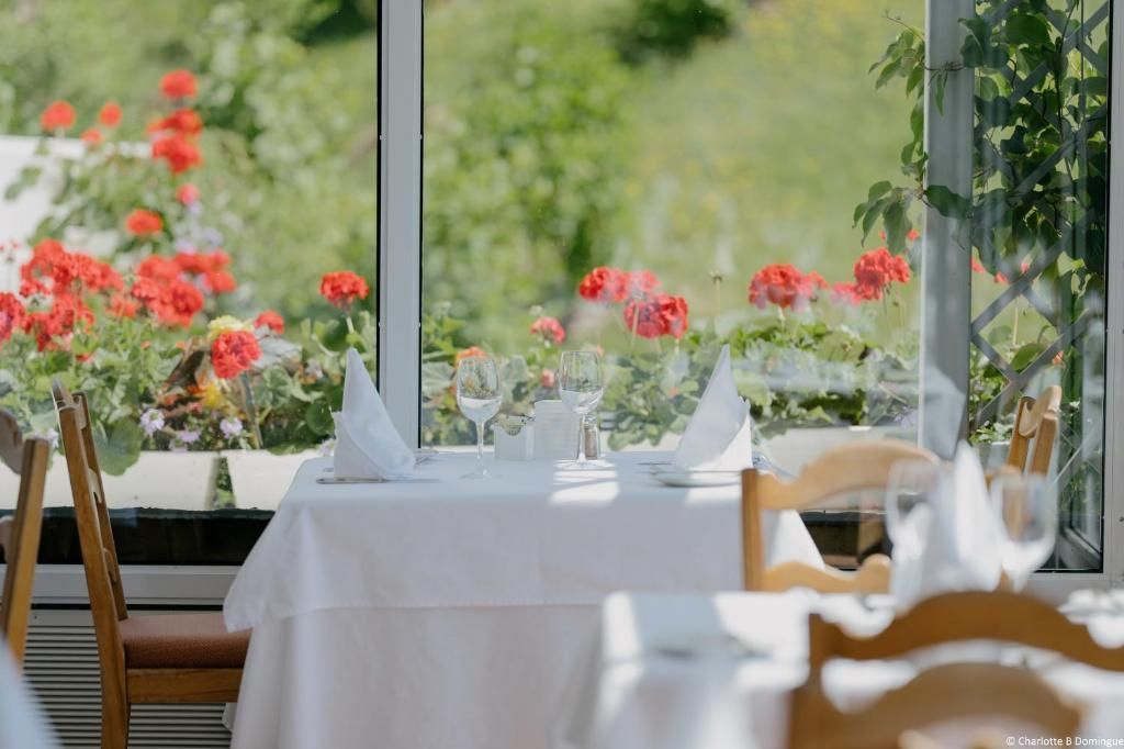 Een elegante restauranttafel bij een groot raam met witte tafelkleden en rode bloemen buiten.
