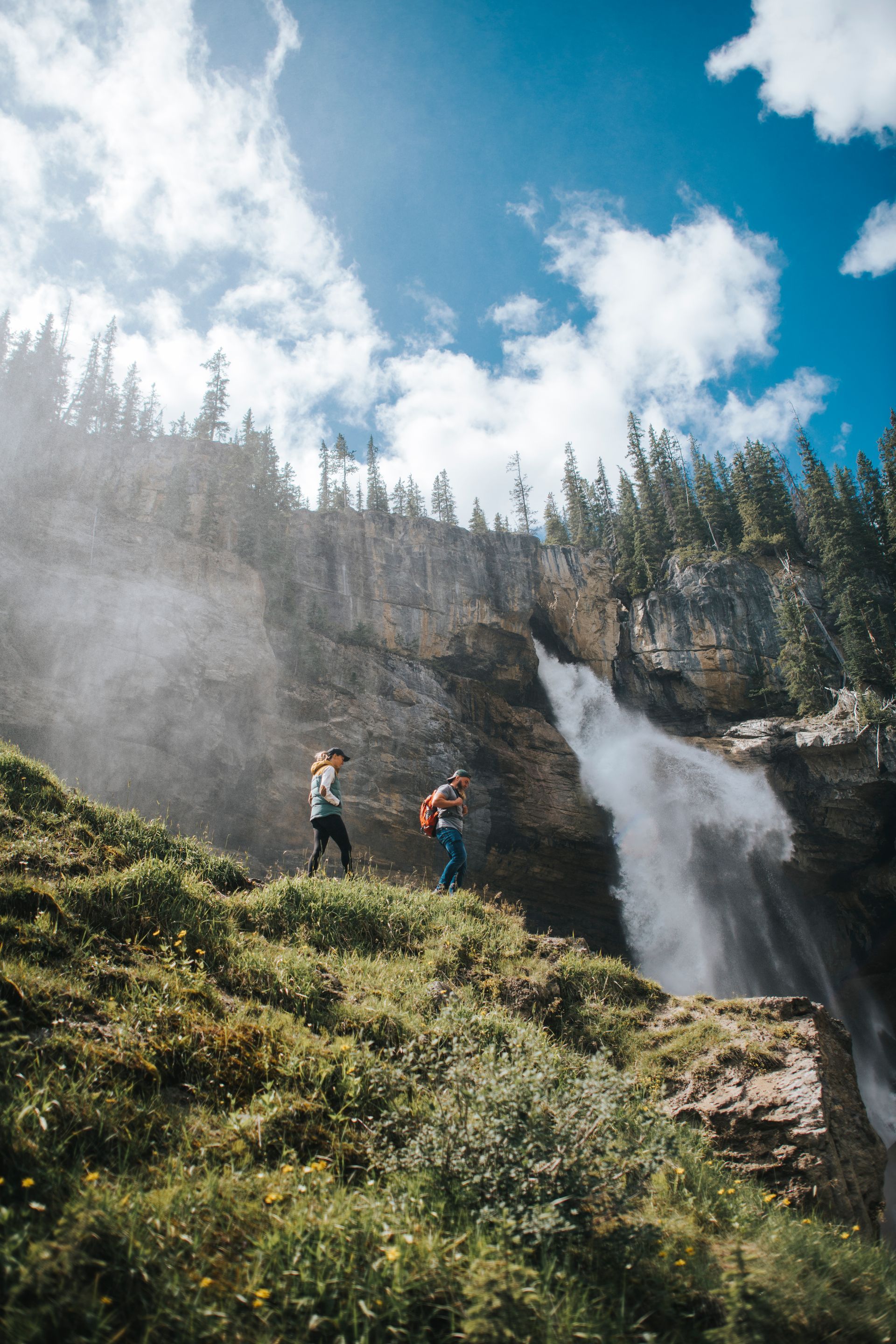 Twee wandelaars op een mistig pad nabij de Panther Falls aan de Icefields Parkway onder een blauwe hemel.