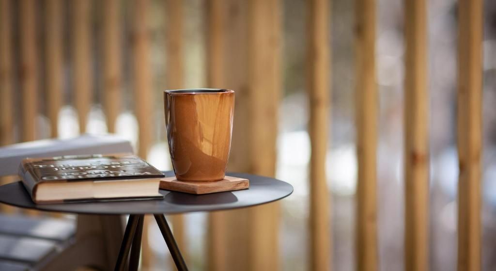 Een houten beker op een ronde tafel naast een gesloten boek, met wazige verticale houten latten op de achtergrond.
