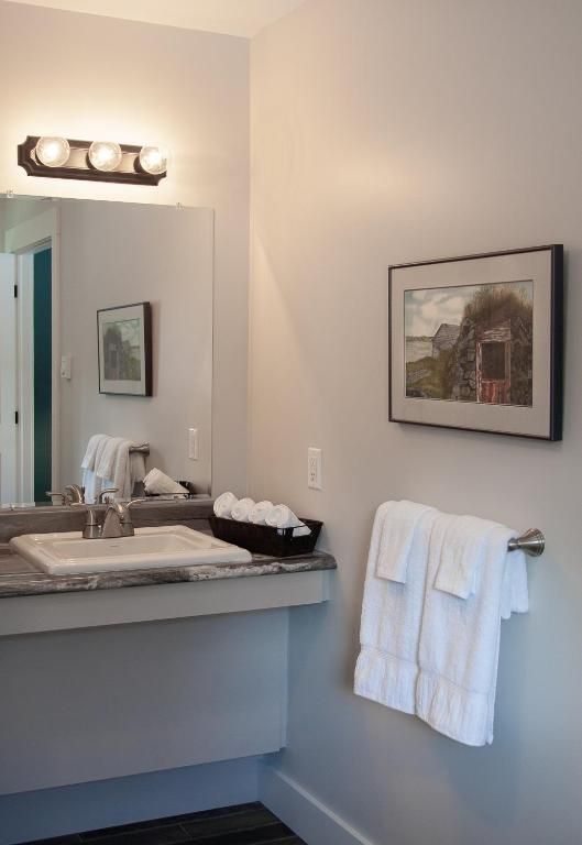 Moderne badkamerkast met spiegel, wandlamp, ingelijste kunst en witte handdoeken aan de muur.