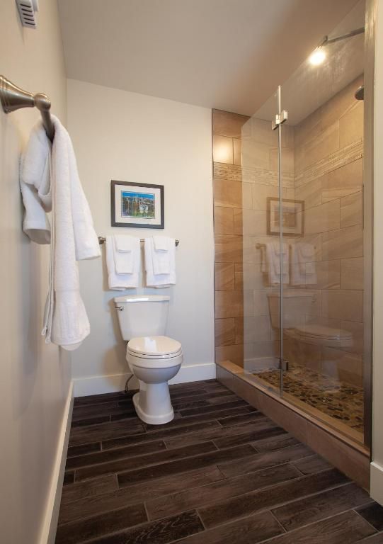 Kleine, moderne badkamer met toilet, glazen douchecabine, witte handdoeken en een donkere vloer met houtlook.
