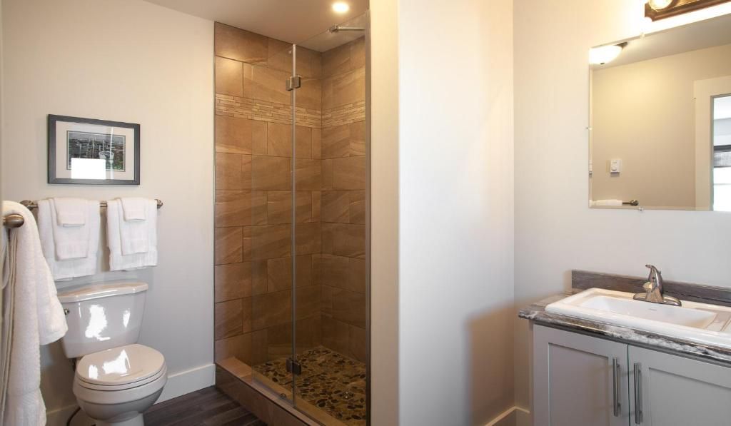 Badkamer met glazen douchecabine, toilet en wastafelmeubel, in een strak beige en wit interieur.
