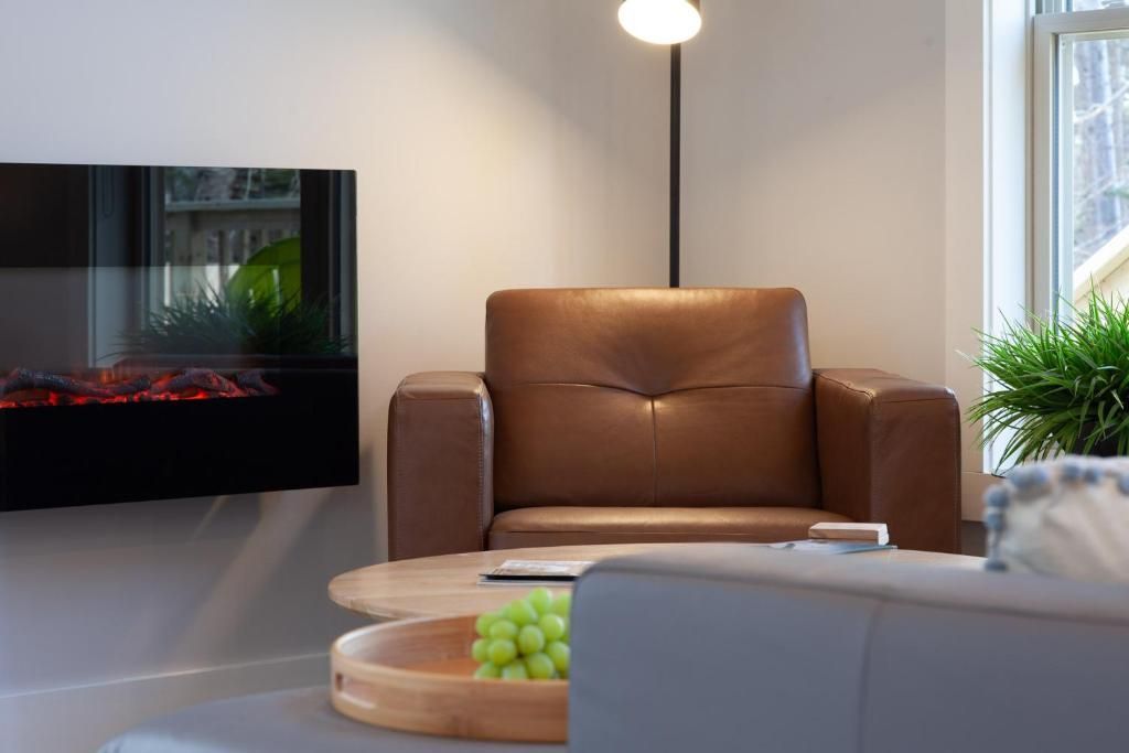 Moderne woonkamer met bruine fauteuil, aan de muur gemonteerde tv, staande lamp en salontafel met groene druiven.
