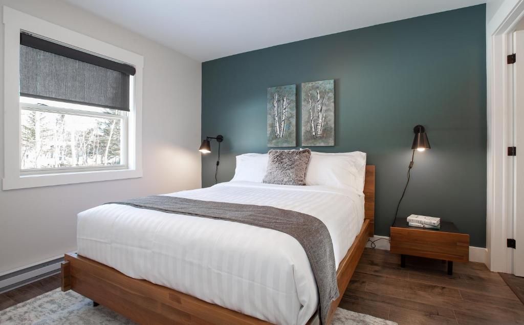Moderne slaapkamer met een turquoise accentmuur, wit beddengoed, een houten bed en twee nachtlampjes.
