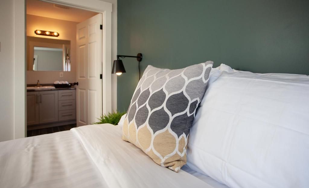 Slaapkamer met wit bed, kussen met patroon, turquoise muur en een open deur naar een badkamer met verlichte make-upspiegel.