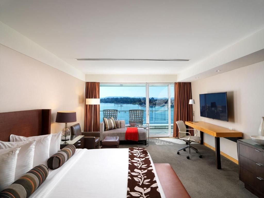 Moderne hotelkamer met twee eenpersoonsbedden, een bank, een bureau en een balkon met uitzicht op de oceaan bij zonsondergang.