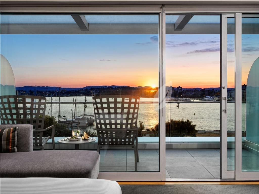 Modern terras met bank en stoelen, met uitzicht op de zonsondergang in de haven door grote glazen deuren.