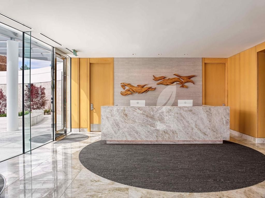 Moderne lobby met marmeren receptiebalie, houten lambrisering, rond tapijt en glazen entree.