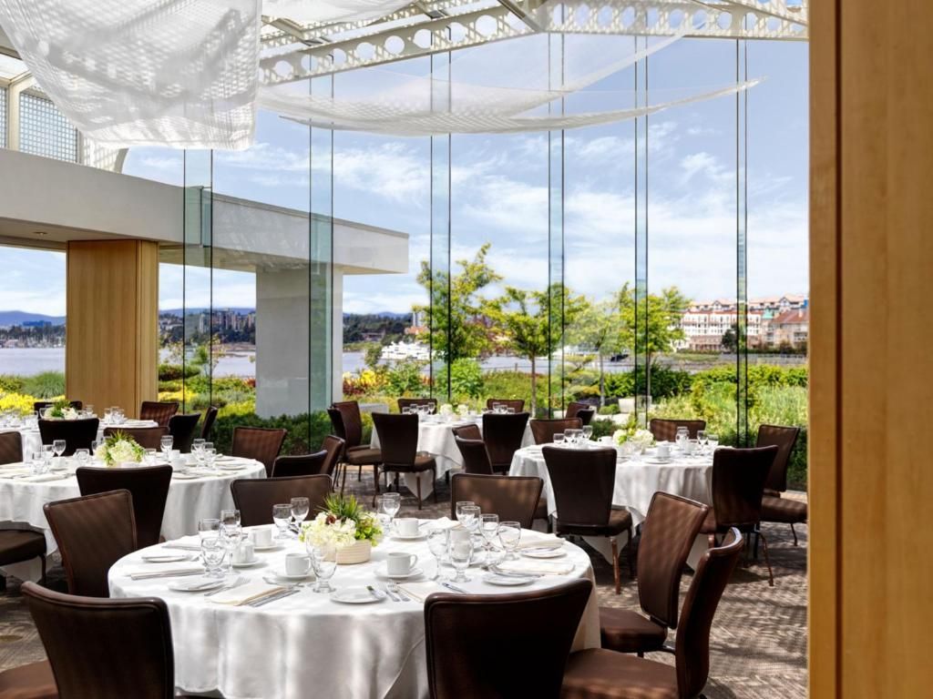 Elegant terras van het restaurant met tafels met witte tafelkleden, donkere stoelen en uitzicht op de tuin onder een overkapping.