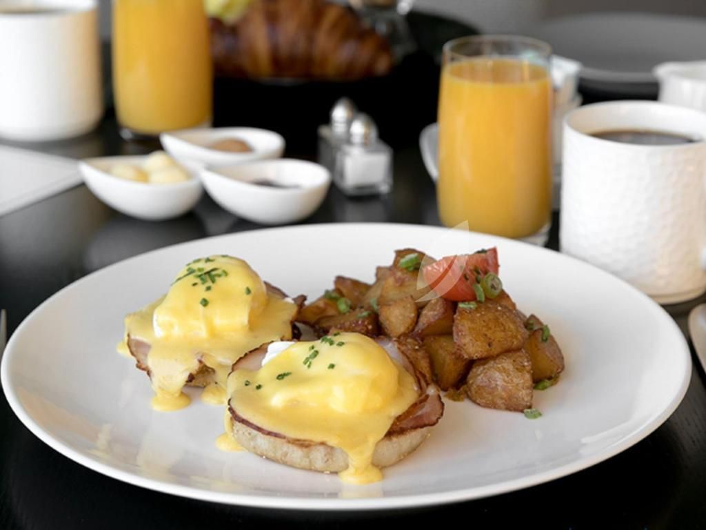Eggs Benedict met aardappelen op een wit bord, geserveerd met sinaasappelsap op de ontbijttafel.