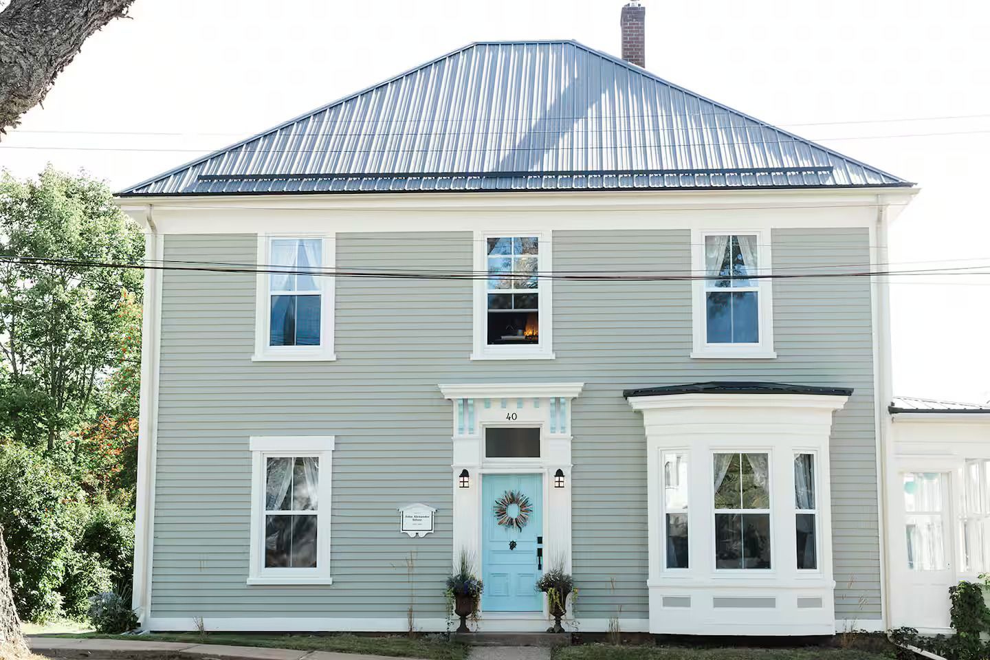 Lichtgrijs huis met twee verdiepingen, een blauw dak en een blauwe voordeur, witte kozijnen en een kleine erker.