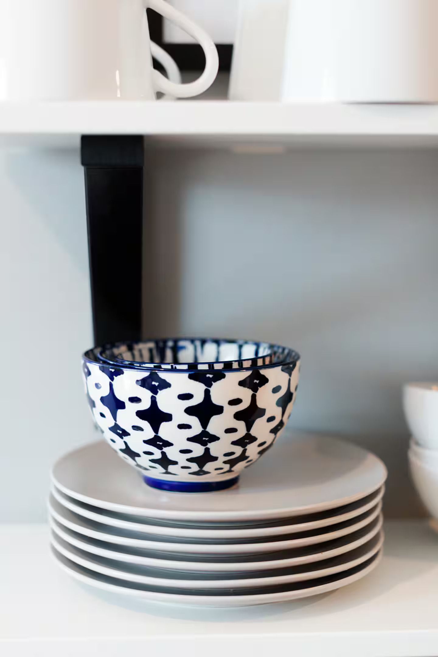 Een stapel witte borden met een blauw-wit patroon kom op een plank.