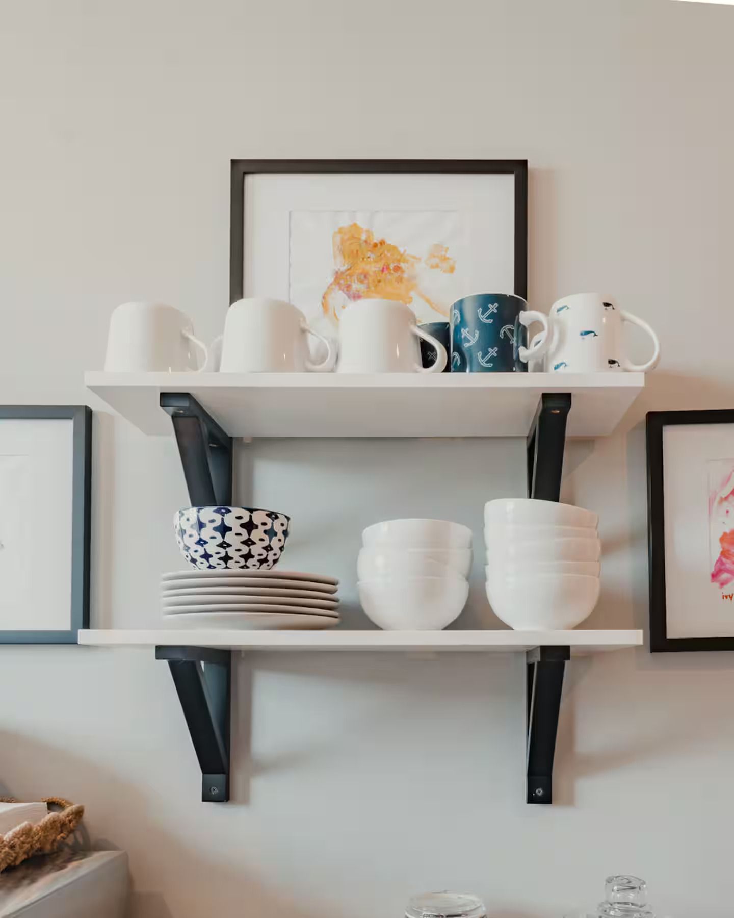 Wandplanken met gestapelde witte en gedessineerde kopjes en schalen in een keuken of eetkamer.