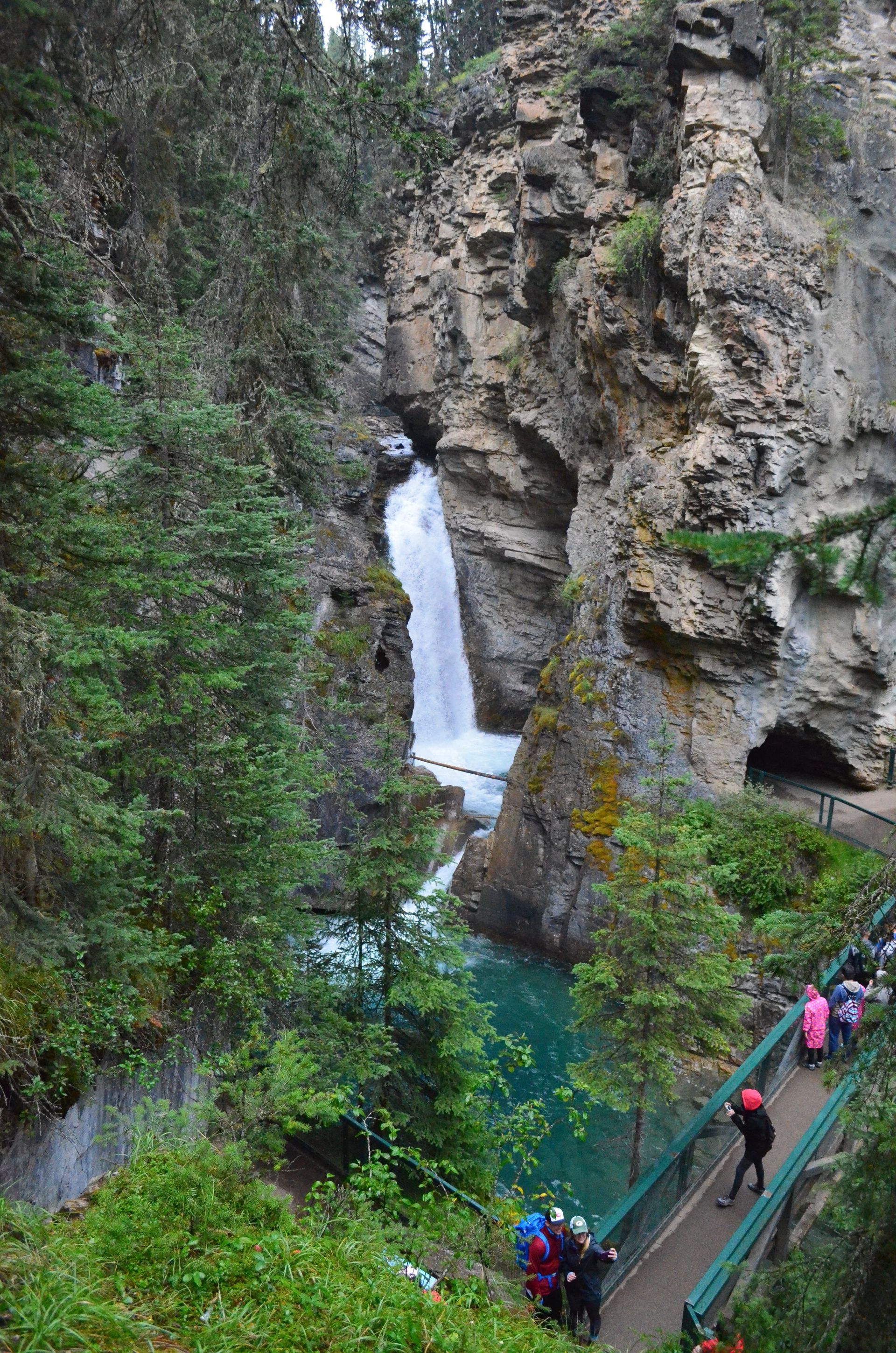 Wandelaars op een houten pad naast een waterval in een steile, groene kloof van Johnston Canyon in Banff National  Park