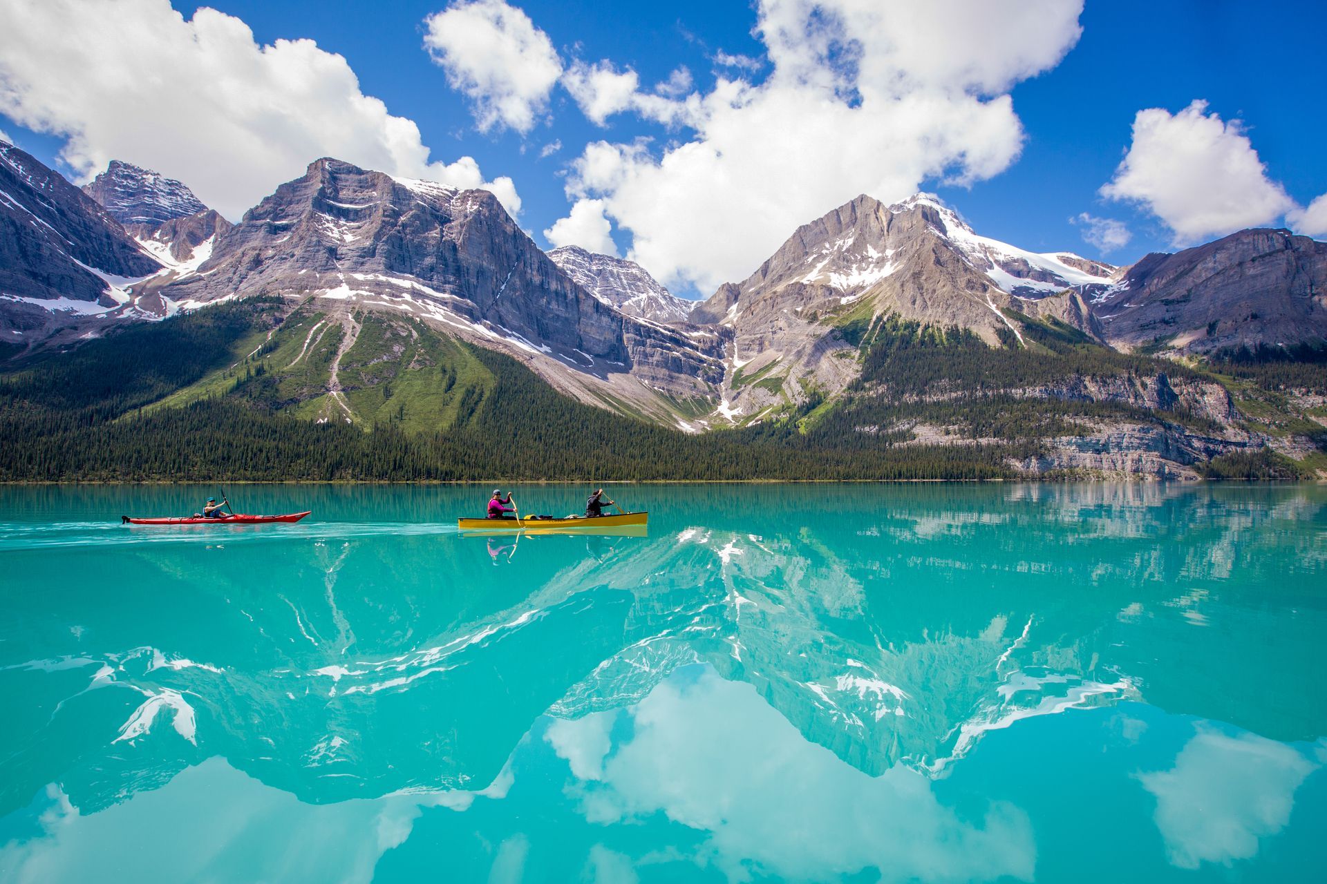 Maligne Lake in Jasper National Park  met kajaks, besneeuwde bergen en een bewolkte hemel die in het water weerspiegeld wordt.