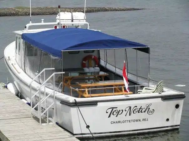 Een witte boot genaamd Top Notch ligt aangemeerd aan een pier, met een blauwe overkapping en een rivier op de achtergrond.