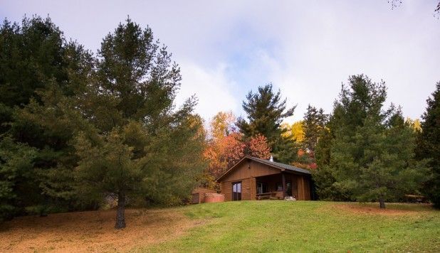 Een blokhut in het bos met een overdekte veranda, gelegen naast een open grasveld in de herfst.