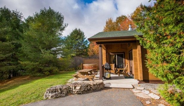 Houten veranda met stoelen, stenen vuurplaats en herfstbomen in een aangelegde tuin.