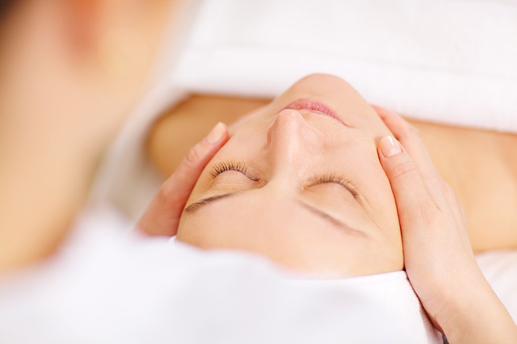 Een persoon die een gezichtsmassage krijgt met handen op het voorhoofd en de slapen in een spa-omgeving.