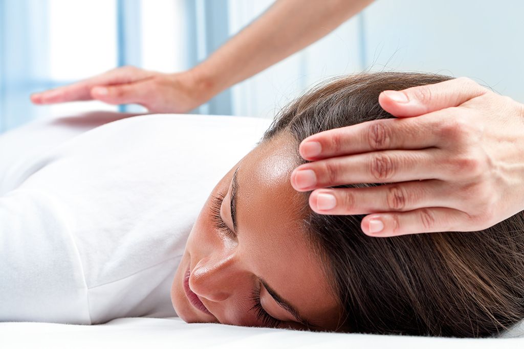 Vrouw ligt op haar buik tijdens een hoofdmassage in een spa, waarbij handen zachtjes op haar slaap drukken.