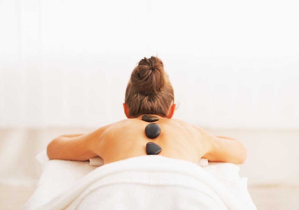 Persoon krijgt een rugmassage met warme stenen op een witte massagetafel.