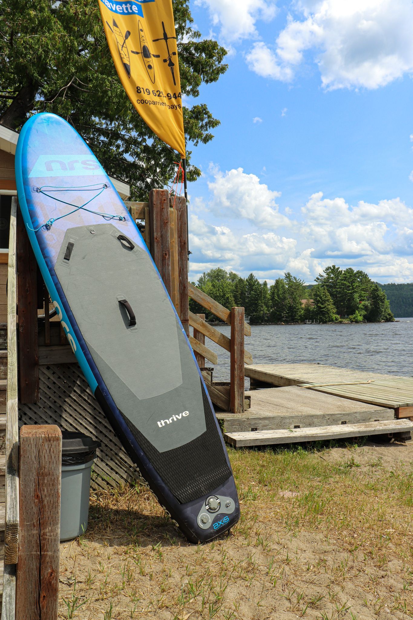 Stand-up paddleboards die tegen een steiger aan het meer leunen onder een blauwe hemel.