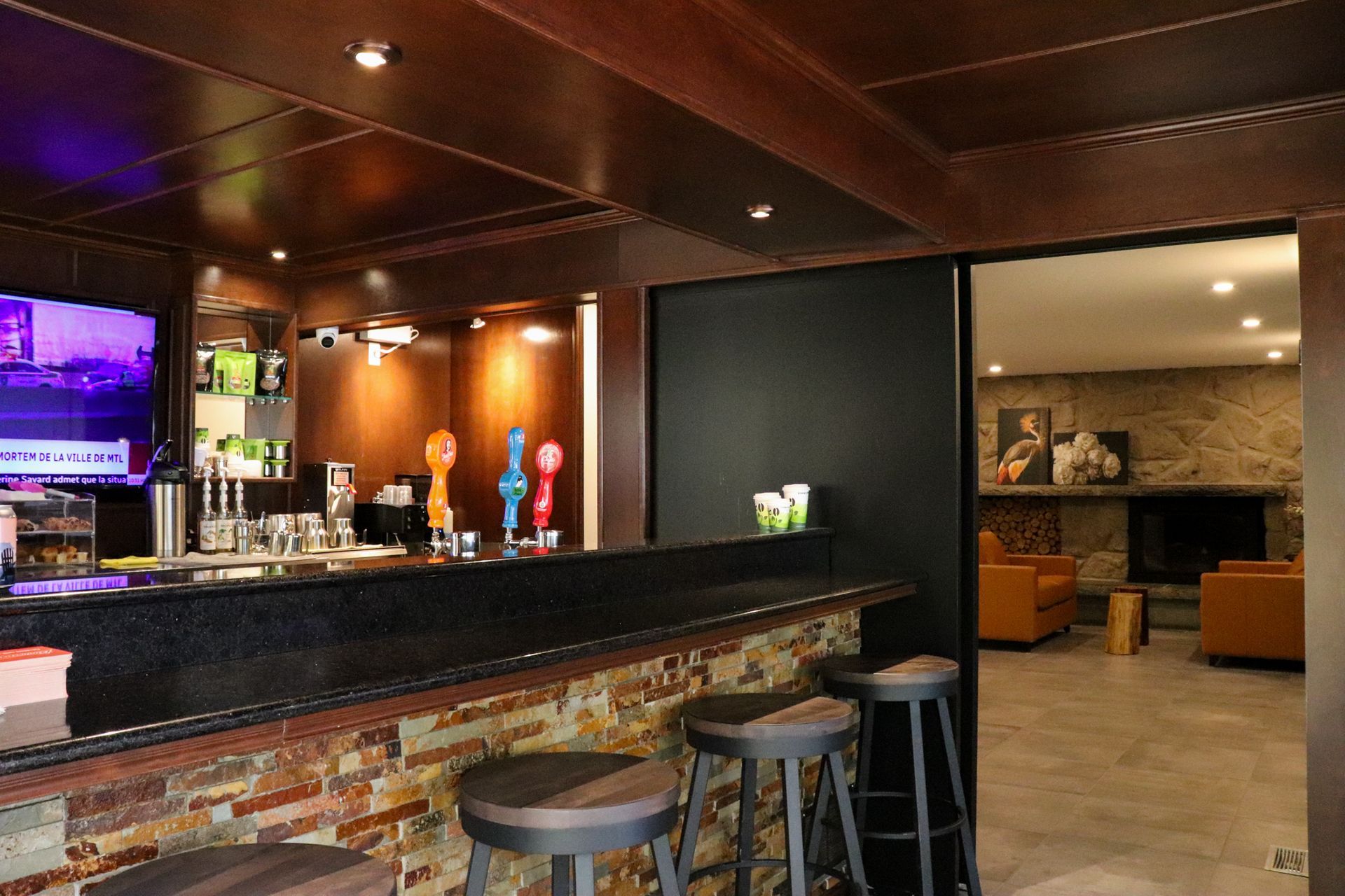Een schemerig verlichte bar met een granieten toonbank, barkrukken, biertaps en een loungehoek op de achtergrond.