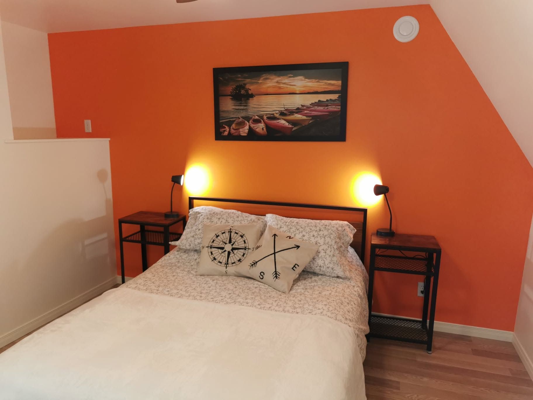 Slaapkamer met oranje muren, een bed, nachtlampjes en ingelijste kunstwerken aan de muur.