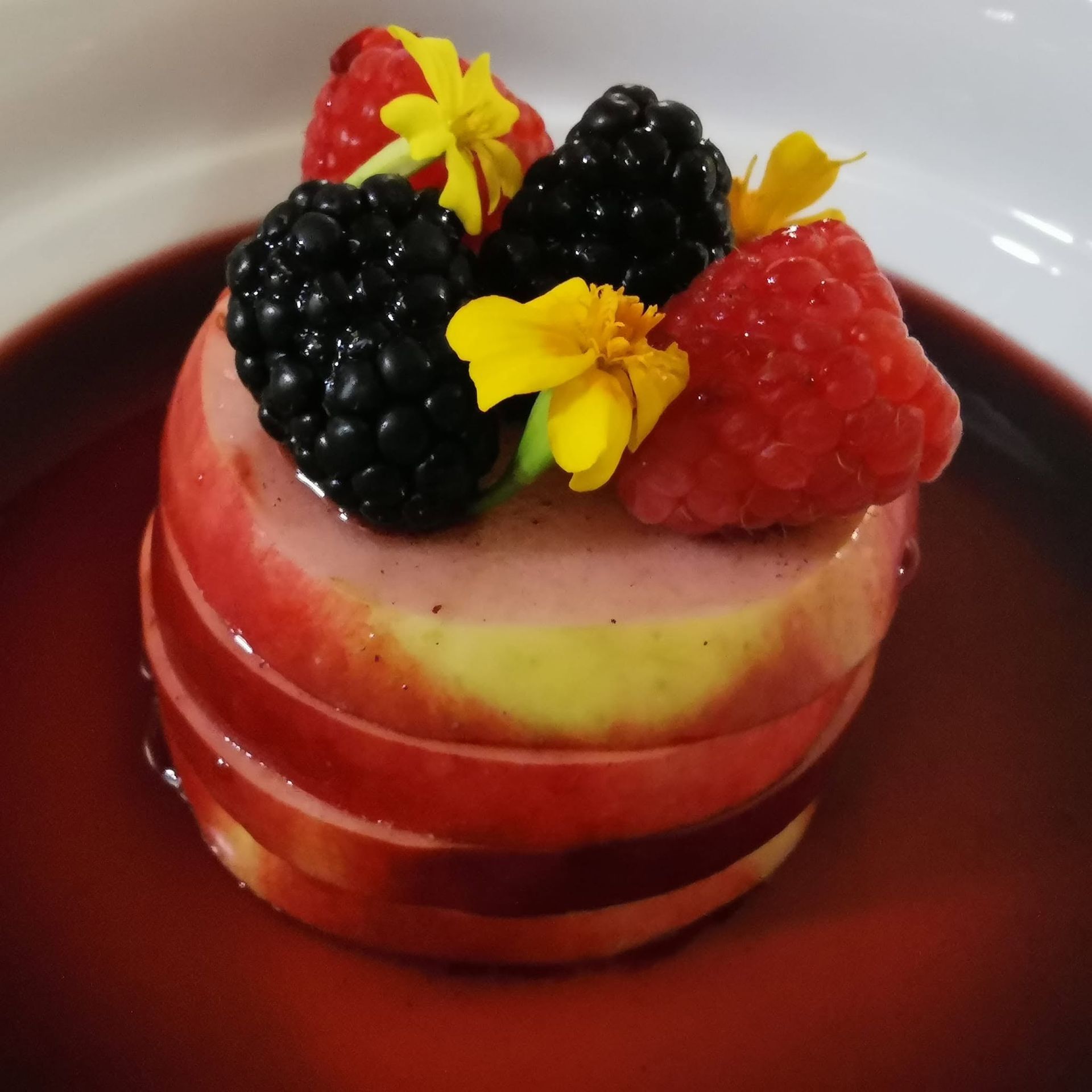 Gelaagd bessendessert met frambozen, bramen en gele bloemen in een rode saus.