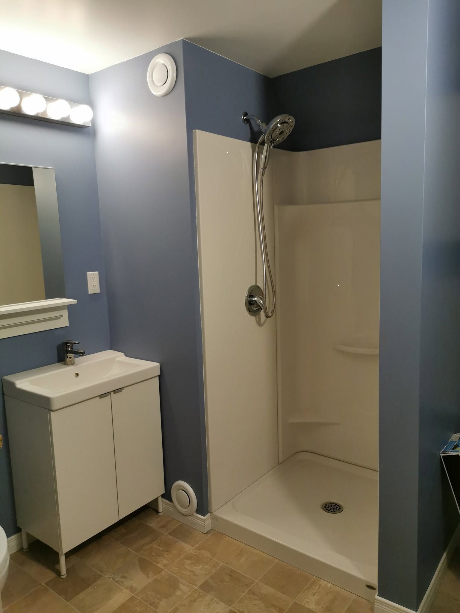 Badkamer met blauwe muren, witte douchecabine, wastafelmeubel en spiegelverlichting.