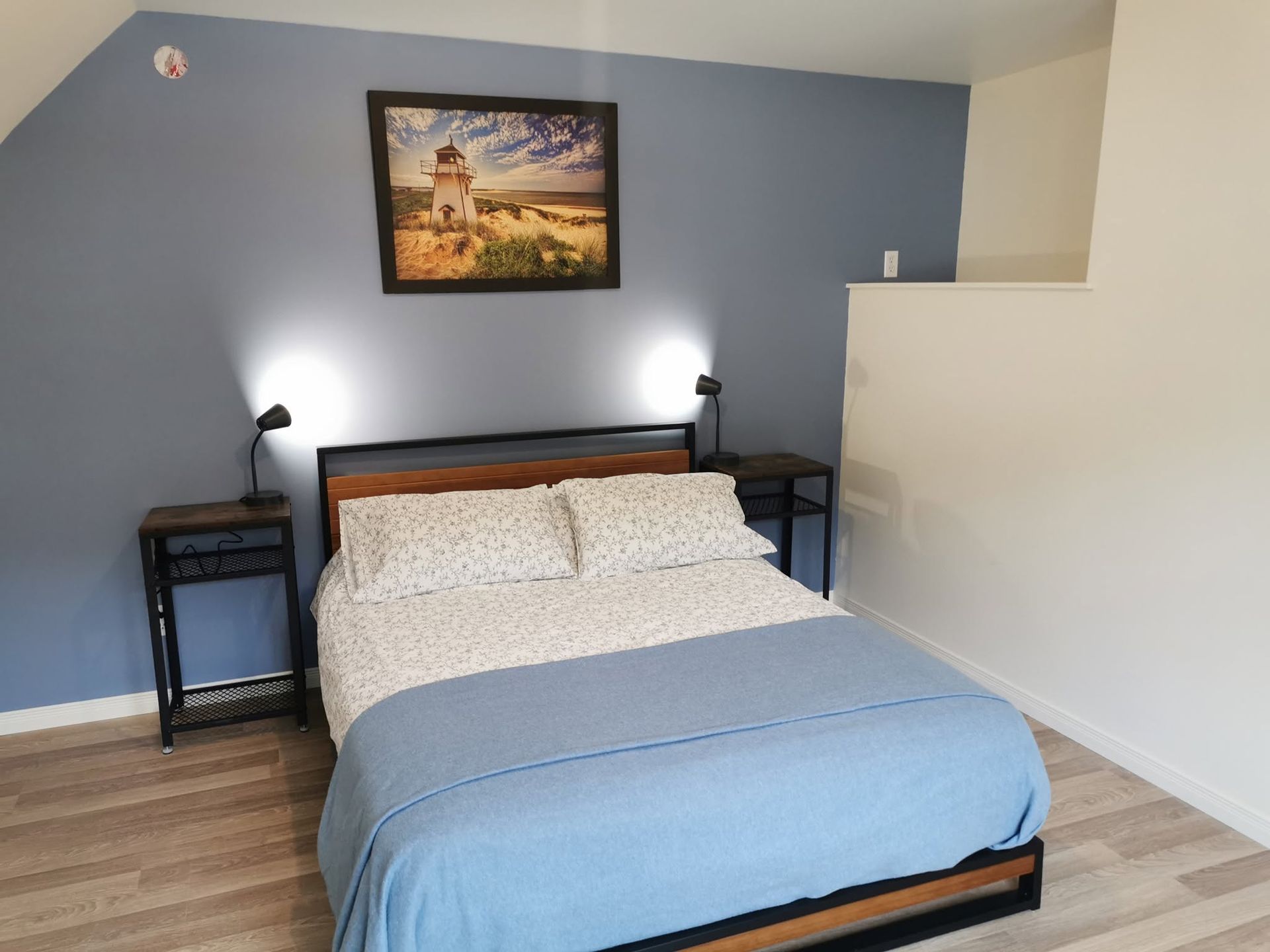 Kleine slaapkamer met een opgemaakt bed, een blauwe accentmuur, nachtkastjes, lampen en ingelijste kunstwerken aan de muur.