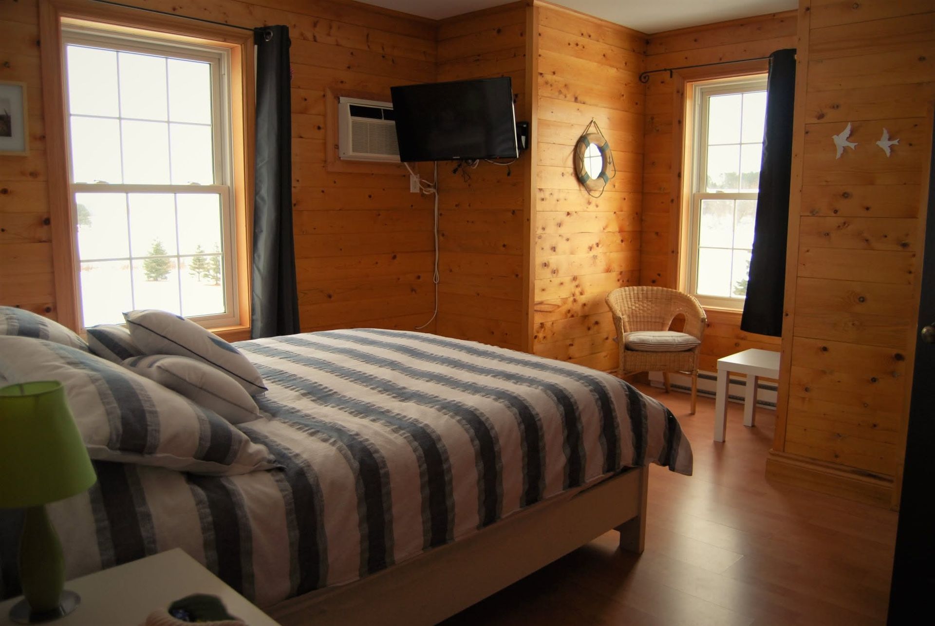 Slaapkamer met houten lambrisering, een gestreept bed, een aan de muur gemonteerde tv, een raam en een kleine stoel.