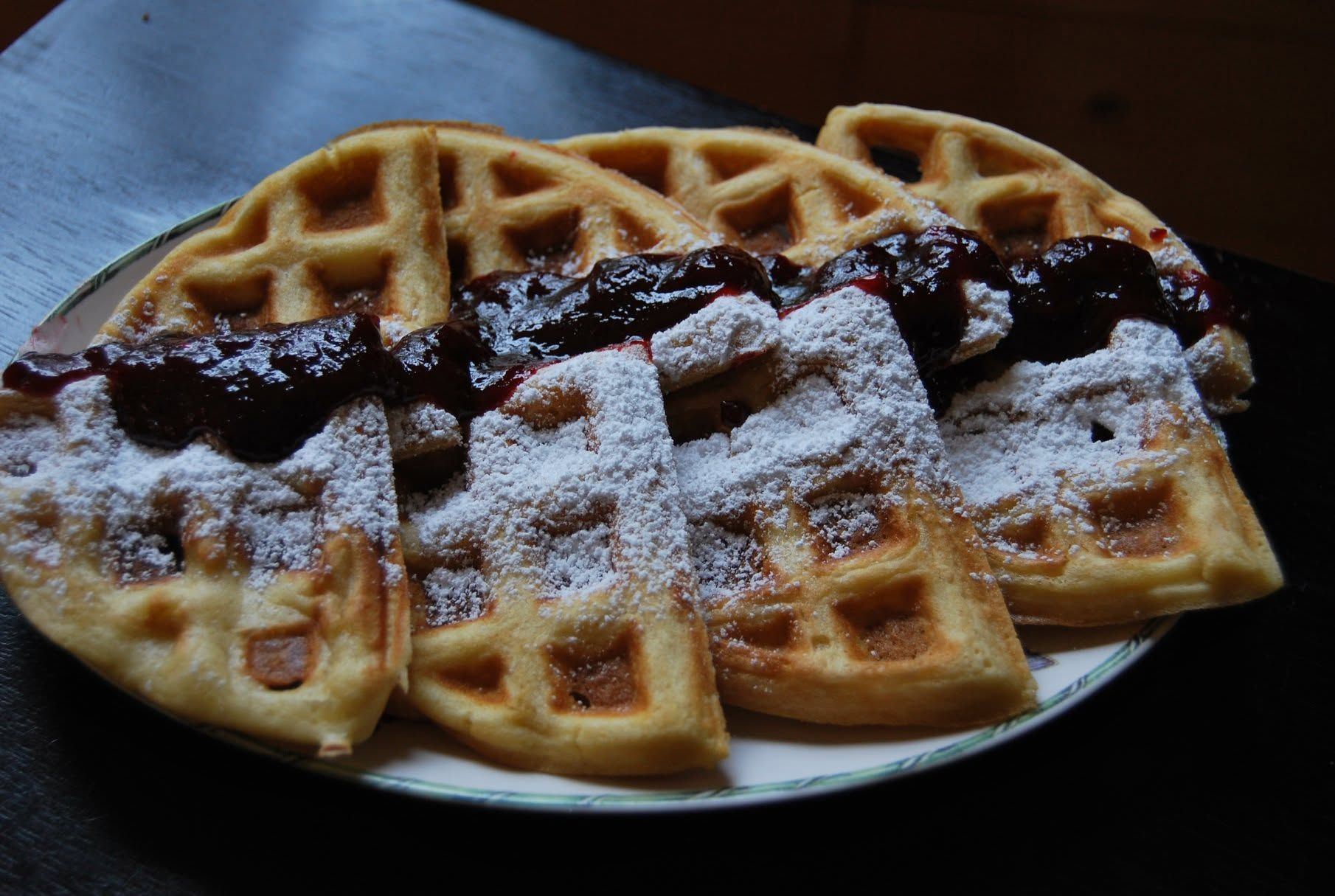 Een bord wafels overgoten met donkere siroop en poedersuiker.