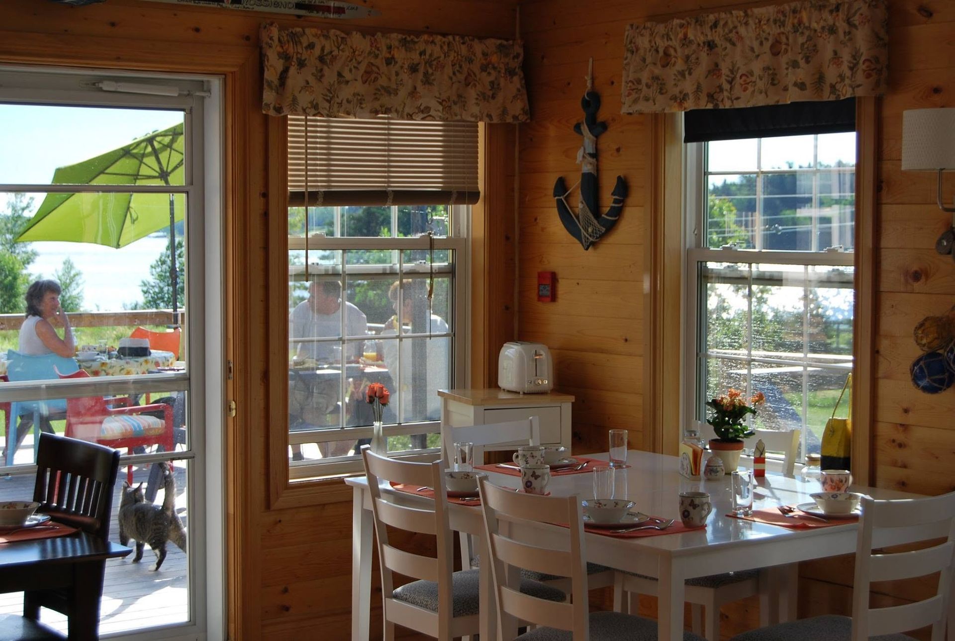 Gezellige eetkamer met witte tafel, stoelen, gordijnen met bloemenprint en uitzicht op de patio door grote ramen.
