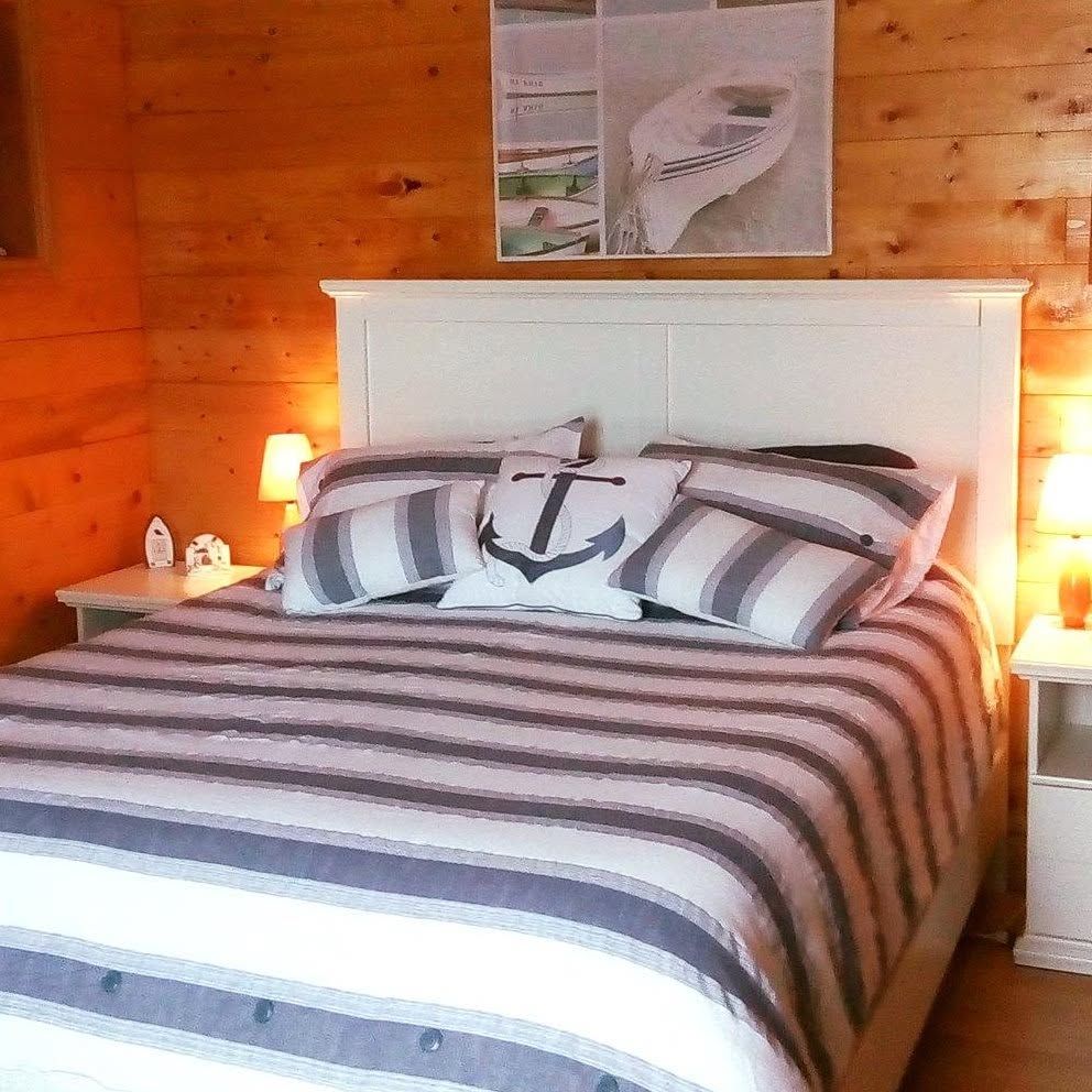 Gezellige slaapkamer met een wit bed, gestreept beddengoed, houten lambrisering en warme nachtlampjes.