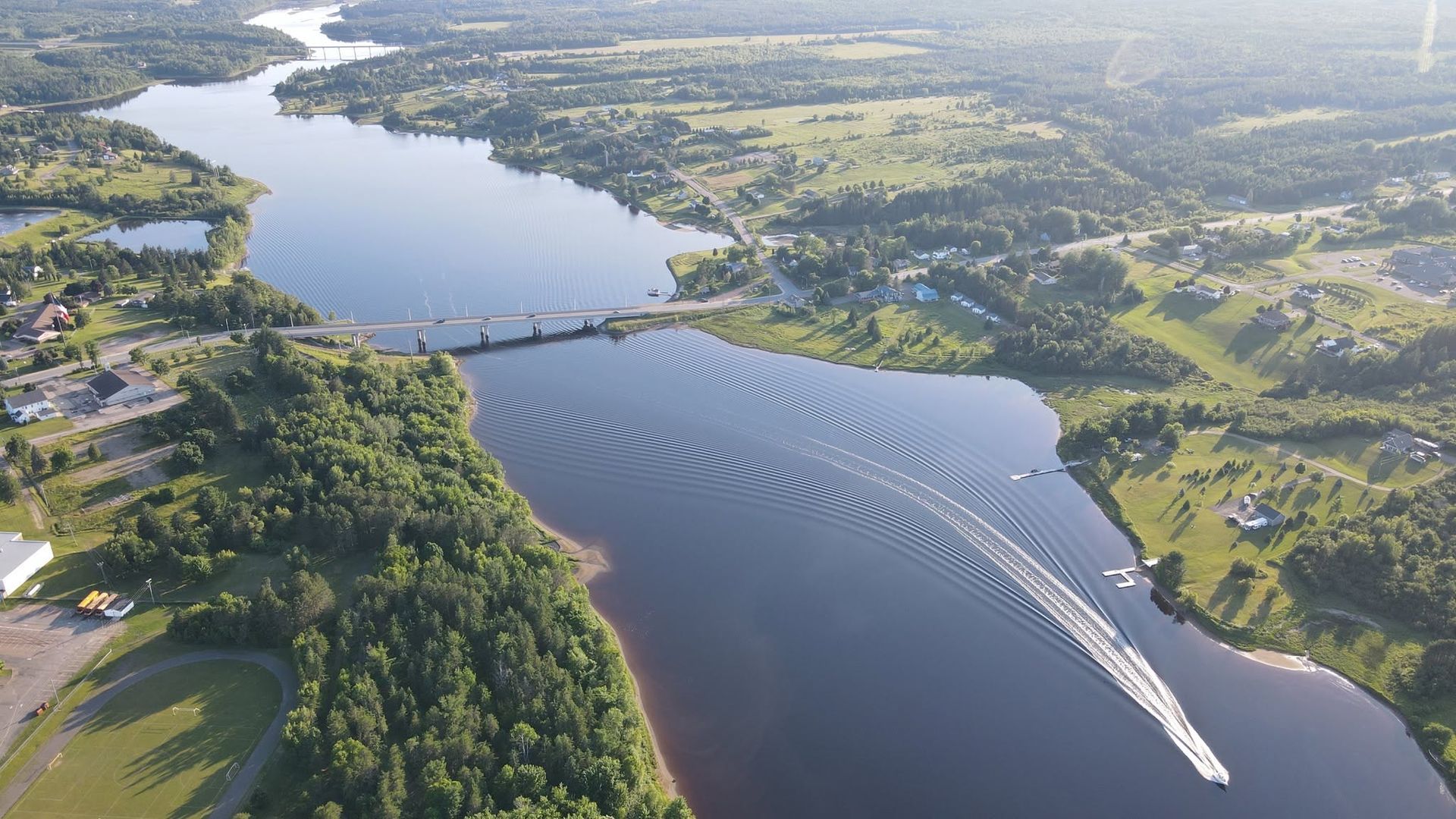 Luchtfoto van een brede rivier met een brug, boten en groene heuvels langs beide oevers.