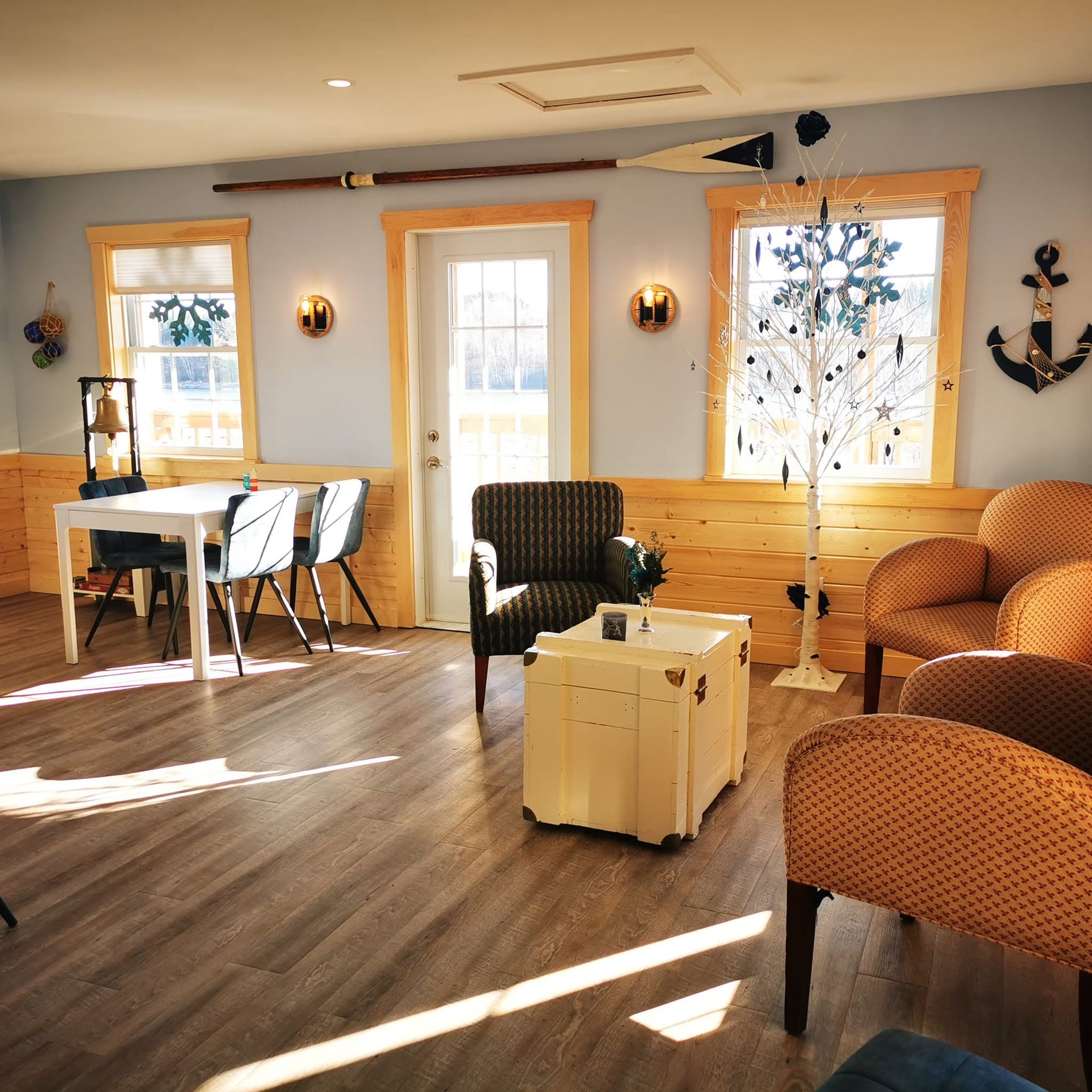 Lichte woonkamer met oranje stoelen, witte tafel, houten vloer en zonlicht dat door de hoge ramen naar binnen schijnt.