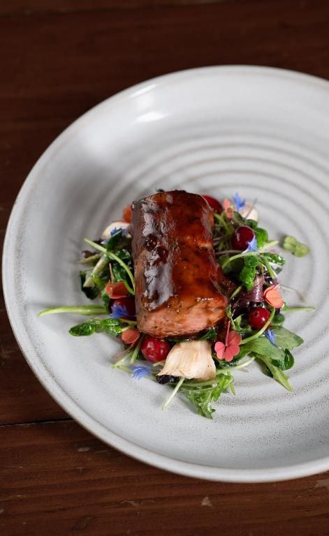 Gebakken zalm op een wit bord met rucola, granaatappelpitjes en saus.