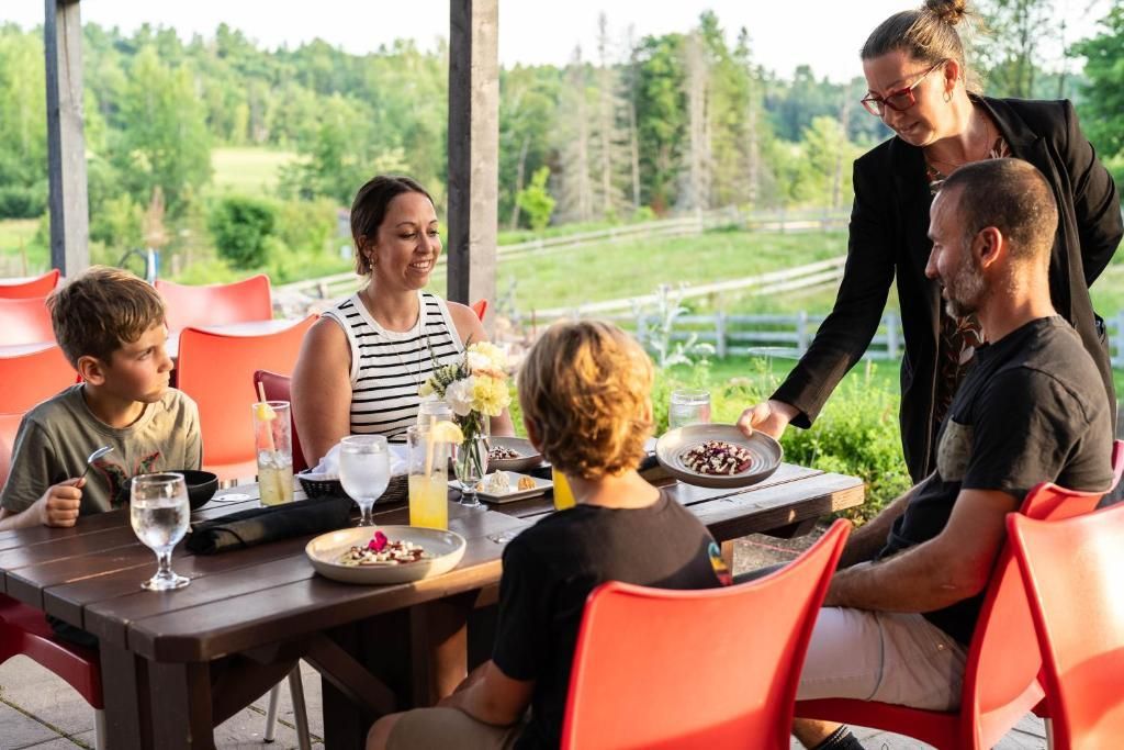 Mensen dineren buiten aan een tafel, terwijl een ober het eten serveert op een terras aan het water.