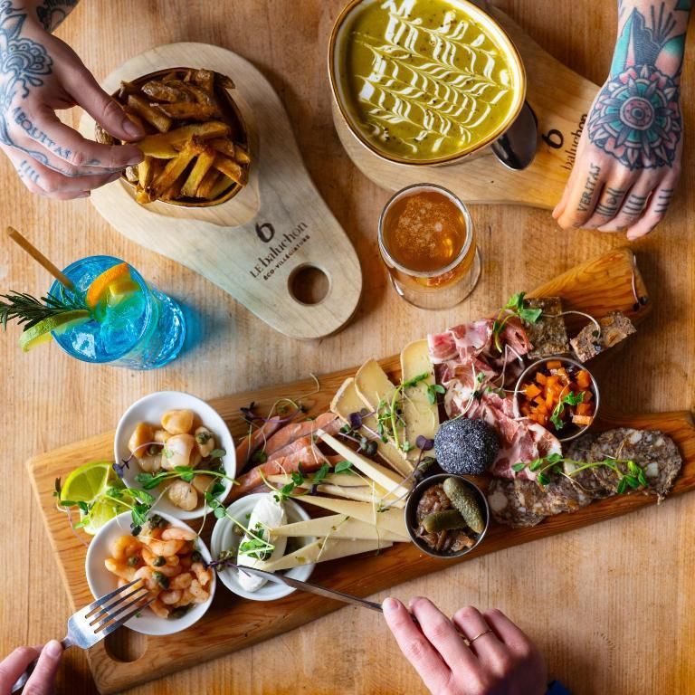 Bovenaanzicht van een tafel met gedeelde gerechten, drankjes, friet en getatoeëerde handen die ernaar reiken.